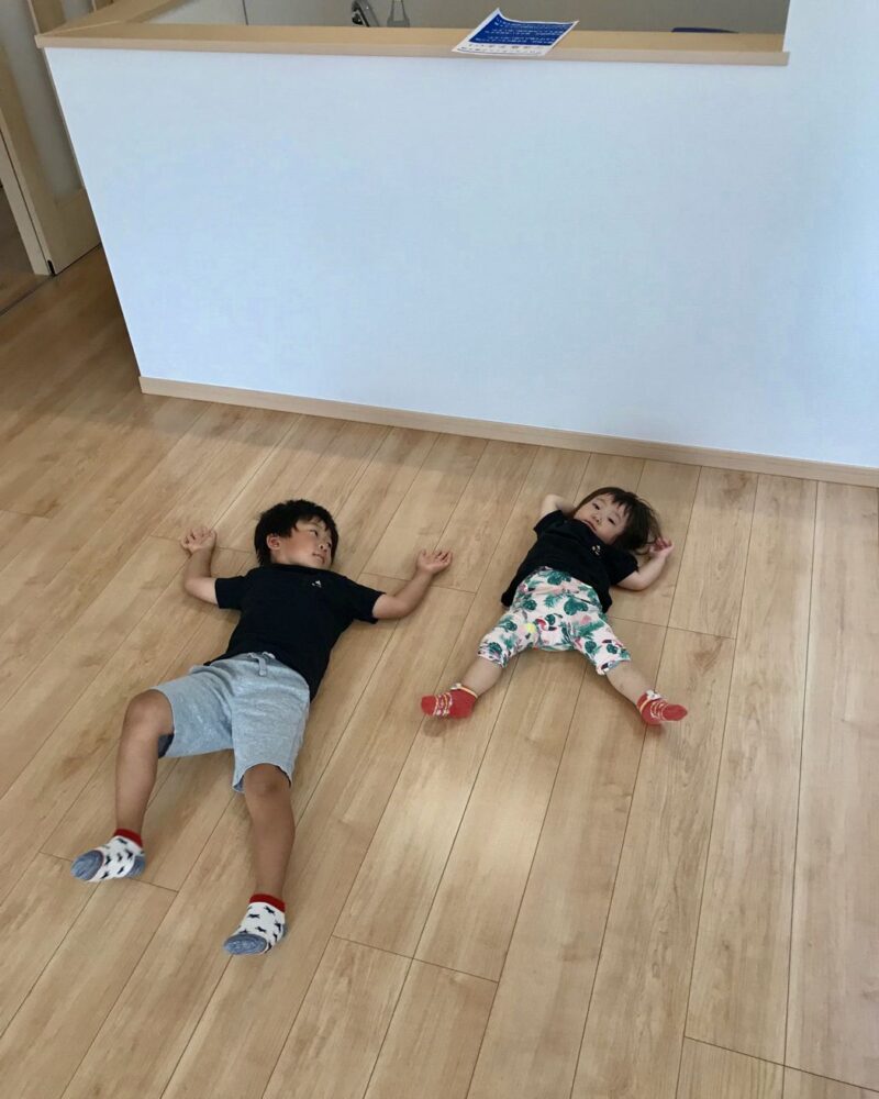 東京都府中市のご新築戸建てで施工後の床に寝ころぶお子さま2人（ガラスフロアコーティング施工後）