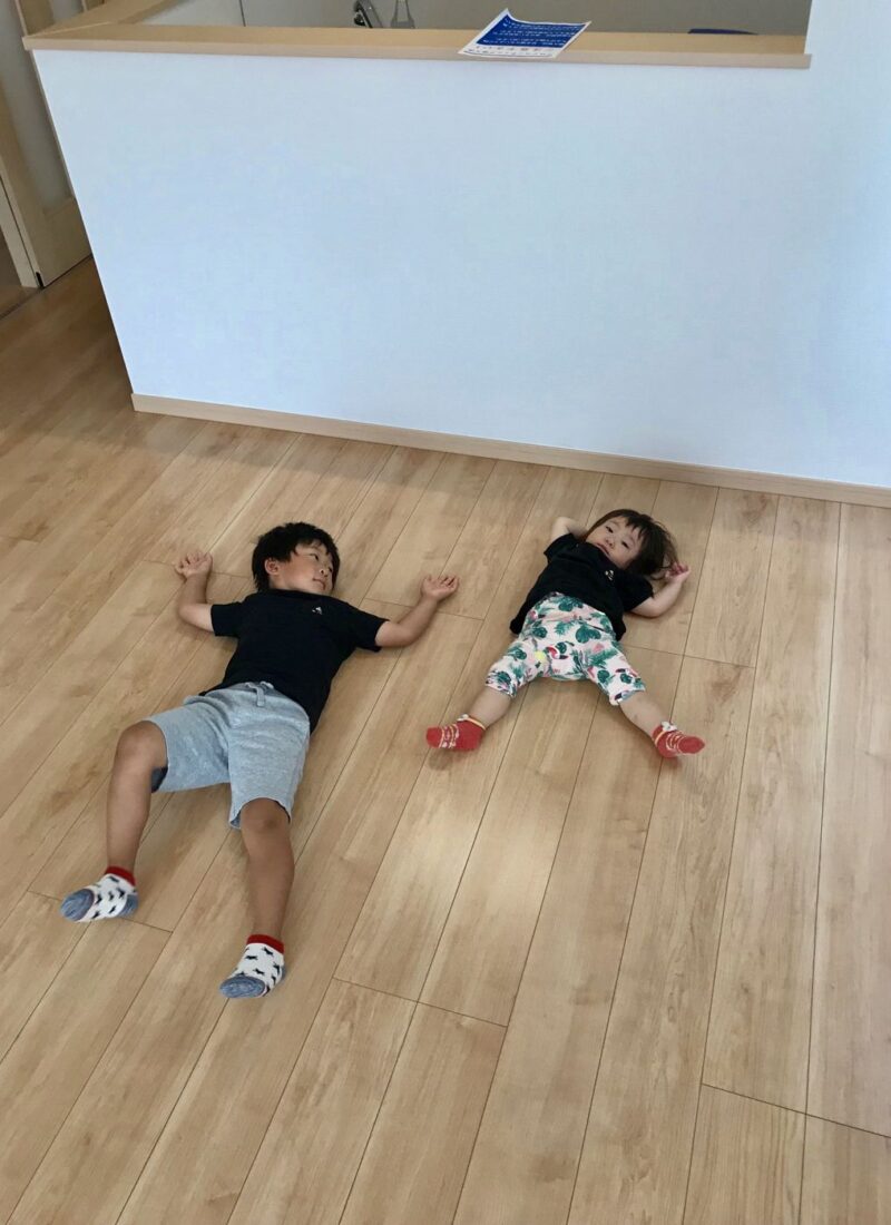 東京都府中市のご新築戸建てで施工後の床に寝ころぶお子さま2人（ガラスフロアコーティング施工後）